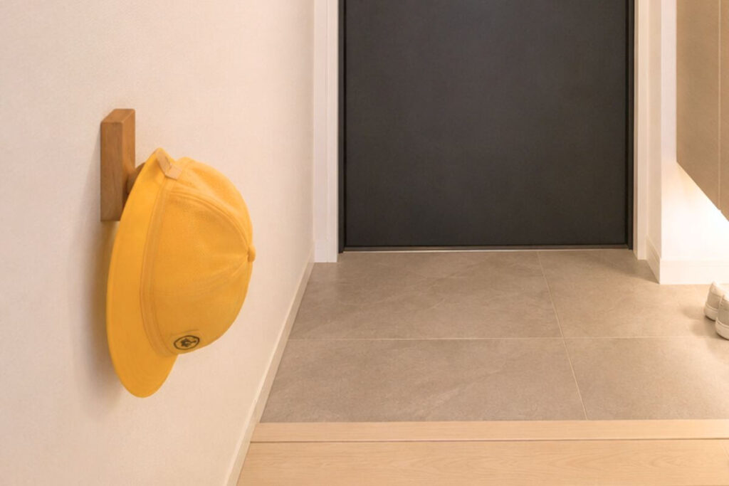 A yellow school hat hanging on a MUJI wall-mounted wooden hook attached to a plasterboard wall in a Japanese entryway.