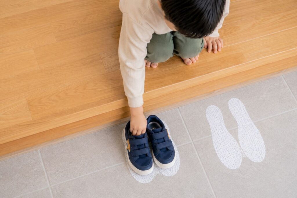 Teaching toddler independence: child placing shoes correctly on floor footprint decals as part of a Montessori-inspired entryway routine.